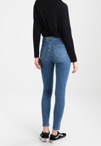 Jeans ajustados de tiro alto en azul con una silueta ceñida, bolsillos traseros y dobladillo deshilachado en los tobillos, combinados con zapatillas Vans negras.