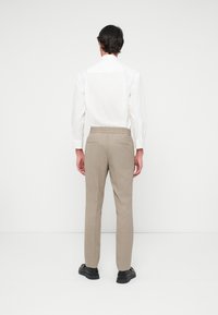 Beige-harmaa housut, joissa on joustava vyötärö ja takataskut, yhdistetty valkoiseen nappipaitaan. Mustat kengät täydentävät asua.