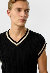 Zwarte gebreide vest met kabelpatroon, V-hals en korte mouwen. Beige gestreepte accenten bij de hals en mouwen. Textuurstof.