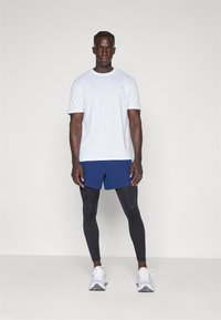 Lichtgrijze shirt met korte mouwen, blauwe sportshorts, zwarte leggings en witte hardloopschoenen. Eenvoudig ontwerp, zachte stof en een getailleerde pasvorm.