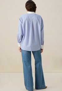 Chemise rayée bleu clair avec un col blanc, à manches longues et à coupe ample, assortie à un jean en denim à jambes larges. Tissu lisse et texturé.
