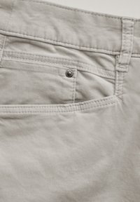 Pantaloni in cotone grigio chiaro con una tasca sul retro dotata di un bottone a pressione argentato, cuciture visibili e una texture morbida.