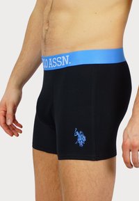 Boxeri din bumbac negri cu un tiv bleu deschis ce prezintă logo-ul "POLO ASSN." și un design brodat al unui călăreț în nuanțe de albastru.