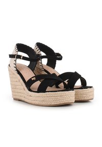 Sandalias de cuña negras con tiras cruzadas de ante negro, plataforma de yute trenzado y parte posterior con un patrón en blanco y negro. Correa de tobillo ajustable.