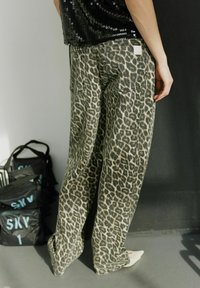 Jeans larges taille haute imprimés léopard en denim. Comprend des poches arrière et une étiquette sur la ceinture. Chaussures non visibles.