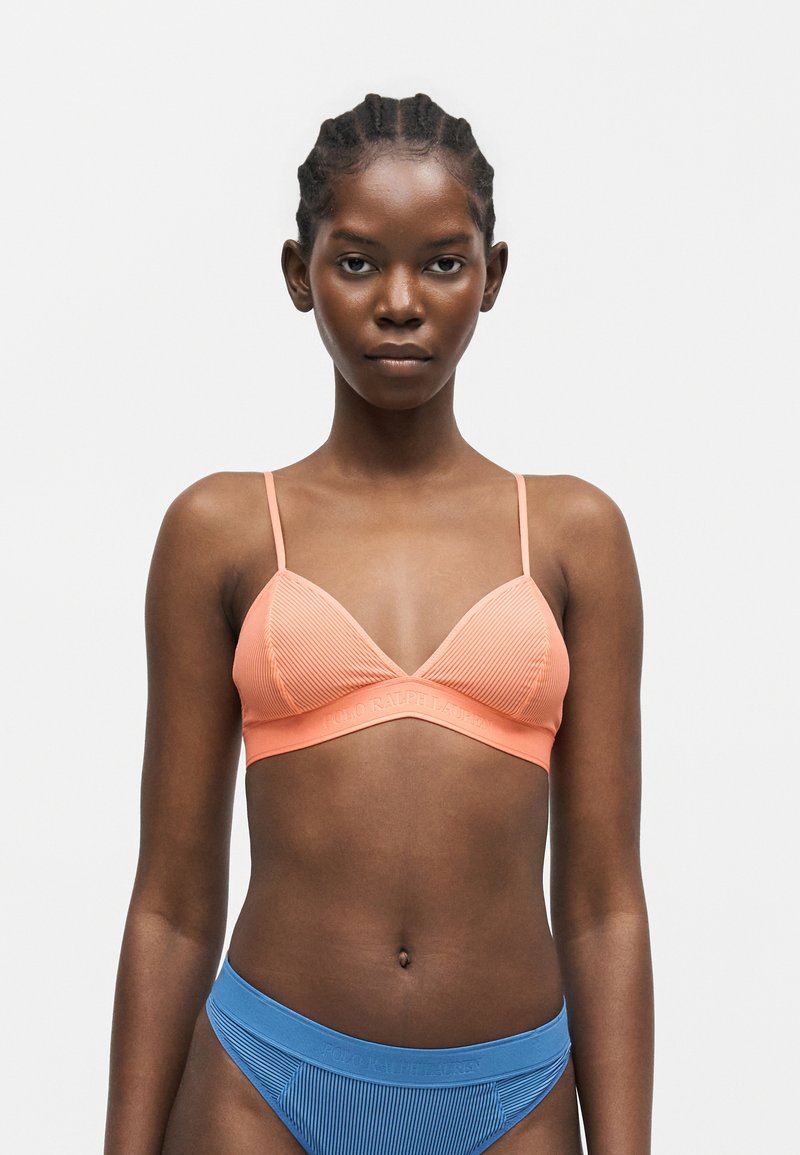 Γυναίκα που φοράει ένα ριμπ πικέ σουτιέν σε ροδακινί χρώμα με λεπτές τιράντες και ριμπ μπλε μπικίνι κάτω μέρος σε απλό λευκό φόντο.