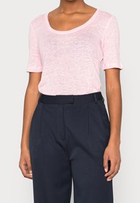 Light pink, short-sleeve T-shirt with a wide scoop neckline, made of a soft, textured fabric. Paired with high-waisted navy trousers.