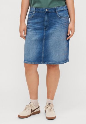 Jupe midi en denim bleu moyen avec une coupe droite, dotée de cinq poches et de quincaillerie en métal. Associée à des baskets beige et des chaussettes légères.