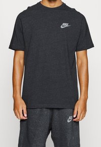 Dark gray cotton T-shirt with short sleeves and crew neck. Features a small reflective Nike logo on the left chest. Smooth texture.