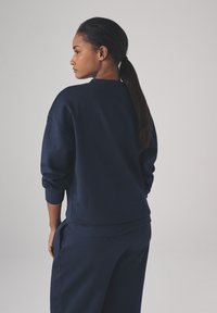 Marineblå sweatshirt med lange ærmer og ribbede manchetter, i en afslappet pasform og rund halsudskæring, vist fra ryggen. Blød tekstur.
