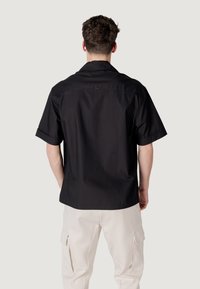 Camiseta de manga corta, negra, en tejido ligero con un corte holgado, que cuenta con un detalle de yugo en la parte posterior y puños enrollados.