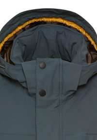 Donkere teal pufferjack met een gestructureerde buitenkant, zwarte knopen en een contrasterende mosterdgele binnenvoering en capuchon.
