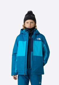 Jachetă izolată albastră și verde-albăstrui cu glugă, cu design în blocuri de culoare, buzunare cu fermoar și logo-ul The North Face pe piept.