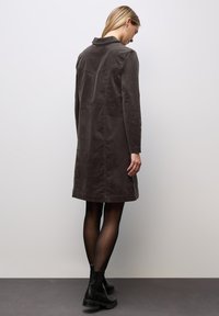 Grijze katoenen coat in een gemengde stof met een getailleerde kraag, lange mouwen en een lengte tot halverwege de bovenbenen. Het heeft een eenvoudig, strak ontwerp met minimale hardware.
