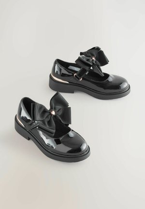 Pantofi Mary Jane din piele lacuită neagră, cu vârful rotund, având o fundă mare din satin negru în față și un accent roz aurit pe tocul pantofului.