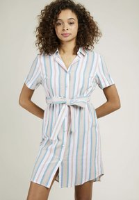 Robe chemise rayée blanche, avec des rayures horizontales bleues, vertes et roses, dotée d'une ceinture nouée et de manches courtes. Fente latérale remarquable.