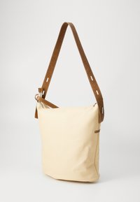 Beige woven fabric shoulder bag with a soft texture; features a brown leather strap with adjustable hardware and a zippered top closure.