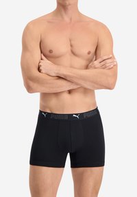 Schwarze Boxershorts aus Baumwollmix, mit einem grauen elastischen Bund, der den Markennamen und das Logo trägt. Eng anliegendes Design mit glatter Textur.