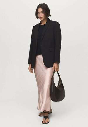 Schwarze Blazer über einem schwarzen Oberteil, kombiniert mit einem glänzenden, pinken Satinrock. Die Accessoires umfassen eine dunkelbraune Handtasche und schwarze Sandalen.