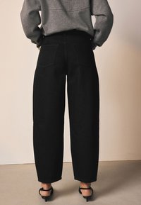 Sorte jeans med vide ben, høj talje og to baglommer, kombineret med en grå sweatshirt. Glat tekstur, syninger og lige snit.