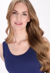 Tyrkysově modrý top bez rukávů s kulatým výstřihem, nošený osobou s dlouhými, vlnitými středně blond vlasy a přirozeným vzhledem líčení.