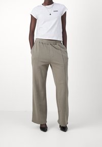 Bílý zkrácený tričko s černým logem "LEVIS", spárované s volnými olivově zelenými kalhotami s elastickým pasem a třepeným lemem.