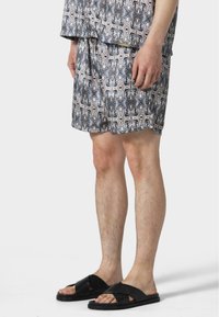 Gemusterte Shorts in Grau, Schwarz und Beige mit einem Kordelzugbund. Kombiniert mit schwarzen Slide-Sandalen mit strukturierten Riemen.