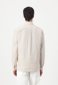 Long-sleeve shirt in off-white fabric with a brown grid pattern, featuring a standard collar and buttoned cuffs, displayed from the back.