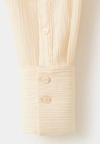 Manche de chemise de couleur crème avec tissu texturé et trois petits boutons ronds sur le poignet et la patte de boutonnage.