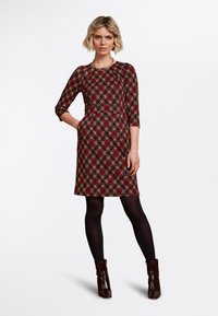 Rotes karierter Kleid mit Dreiviertelärmeln, Rundhalsausschnitt und definiertem Bund. Kombiniert mit schwarzen Strumpfhosen und glänzenden braunen Ankle Boots.