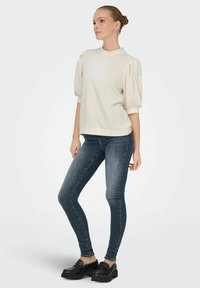 Light beige sweatshirt with short puff sleeves, round neckline, and ribbed hem, paired with dark blue skinny jeans and black chunky loafers.