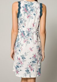 Robe florale avec un fond crème, ornée de fleurs bleues et roses. Conception sans manches avec des accents de dentelle teal aux épaules.