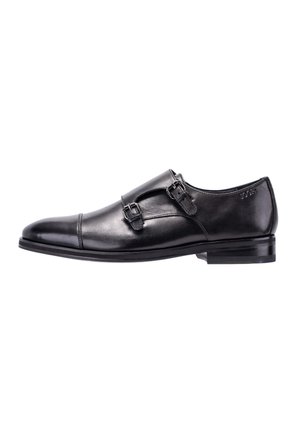 Zwarte leren nette schoenen met dubbele monkriempjes, afgeronde neus en lage gestapelde hak, zijaanzicht op witte achtergrond.
