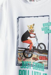 T-shirt en coton blanc avec un graphique vibrant d'un cycliste ayant une tête de tigre, portant un pantalon orange, et des blocs de texte avec "KEEPIN' ROLLIN' ALWAYS" et "JUST GONNA ROLL".