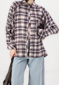 Ruudullinen nappipaita pehmeästä kankaasta sisältää ruskean, violetin ja kerman sävyjä. Siinä on klassinen kaulus ja etutasku.