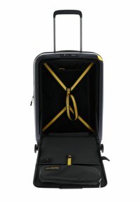 Valise rigide noire avec des accents jaunes. Elle dispose d'une poignée rétractable, de sangles intérieures et de compartiments pour une meilleure organisation.
