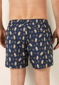 Pantaloni de înot navy cu un model jucăuș de ursuleți de pluș și colaci de salvare, talie elastică și un singur buzunar la spate. Material neted și ușor.