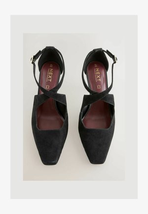 Black suede high-heeled shoes with a square toe. Features cross straps and an ankle buckle. Interior has a maroon lining with brand logo.