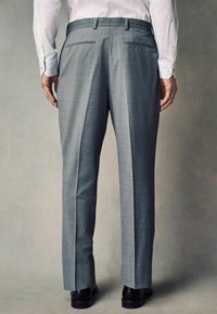 Pantalones grises ajustados con un sutil patrón de cuadro, de corte recto y con bolsillos laterales. La tela tiene una textura suave, combinada con zapatos negros.