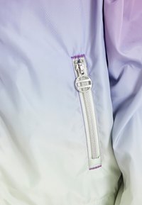 Letvægts gradient vindjakke med en glat farveovergang fra lavendel til hvid, udstyret med en skinnende sølv lynlås og kontrastfarvet lilla syning.