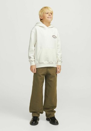 Cremefarbener Hoodie mit einer Fronttasche und braunem, gesticktem Logo, kombiniert mit lockeren olivgrünen Hosen und schwarzen Schuhen. Glatte Stofftextur.