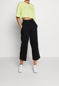 Light green cropped T-shirt with "NIKE" logo; black ribbed wide-leg pants with drawstring and side pockets; white sneakers.