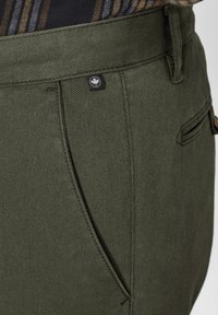 Olive green trousers made of textured fabric, featuring a front pocket design, subtle stitching details, and a small logo tag.