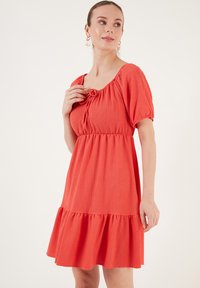 Short-sleeved, knee-length dress in bright orange textured fabric. Features a scoop neckline and gathered waist with ruffle hem.