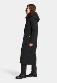 Langer schwarzer Parka mit Kapuze, aus wasserabweisendem Material. Verfügt über Fronttaschen, einen Reißverschluss und eine gerade Silhouette.