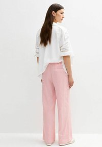 Witte overhem button-up met opgerolde mouwen, gecombineerd met hoog getailleerde lichtroze linnen broek. Glad textuur, relaxte pasvorm, met één achterzak.
