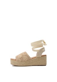 Sandalias de cuña beige con una tira delantera bordada, suela de esparto texturizada y lazos de tela entrecruzados en el tobillo.