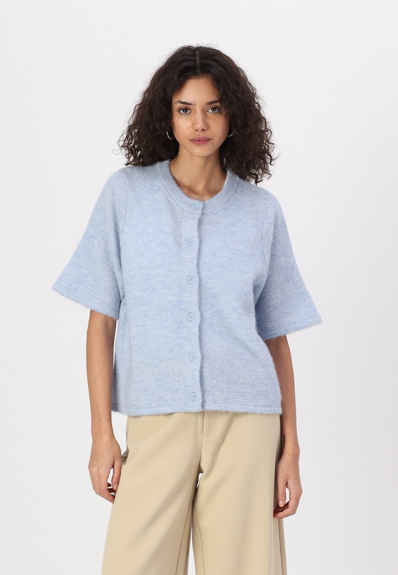Cardigan bleu clair à manches courtes en matière douce et duveteuse. Il présente un col rond et une fermeture à boutons sur le devant.