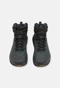 Črne pohodniške čevlje srednje višine z teksturirano zgornjim delom, črnimi vezalkami, Vibram podplatom in ojačano konico. Imajo logo in zapletene šive.