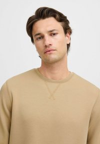 Beige sweatshirt med rund halsudskæring, med teksturerede detaljer ved skuldersømmen og en blød, glat stoffinish.